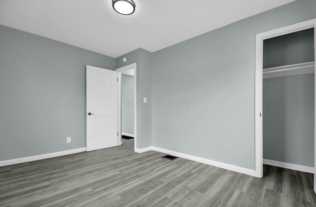 unfurnished bedroom featuring wood finished floors, baseboards, and a closet