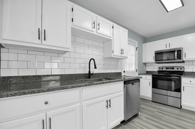 kitchen featuring appliances with stainless steel finishes, a sink, white cabinetry, dark stone counters, and backsplash