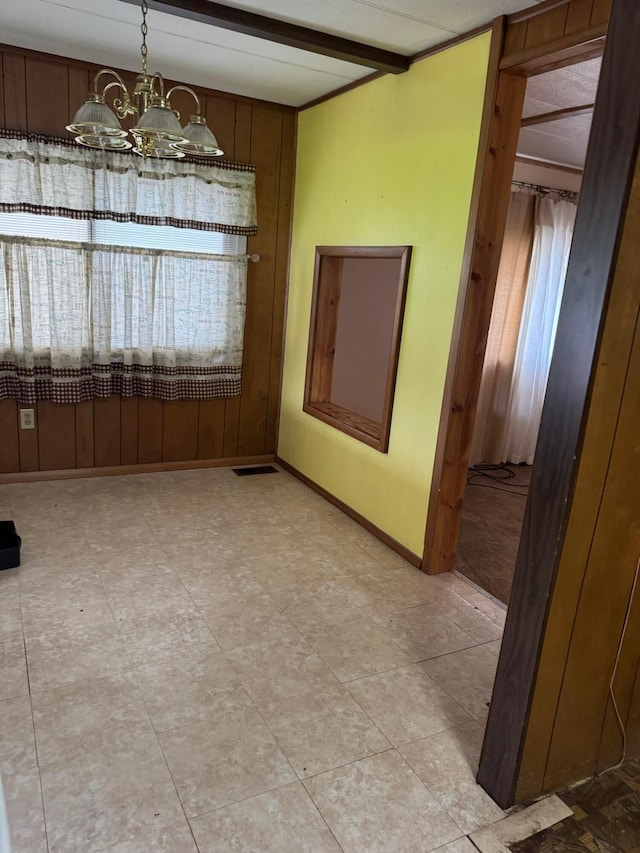 spare room featuring a chandelier, wooden walls, and baseboards