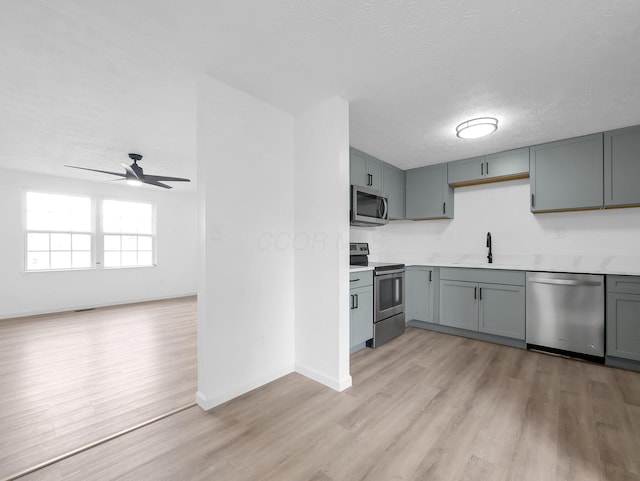 kitchen featuring stainless steel appliances, light wood finished floors, ceiling fan, light countertops, and a textured ceiling