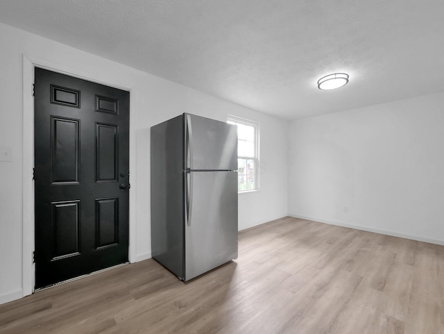 kitchen with freestanding refrigerator, light wood finished floors, a textured ceiling, and baseboards
