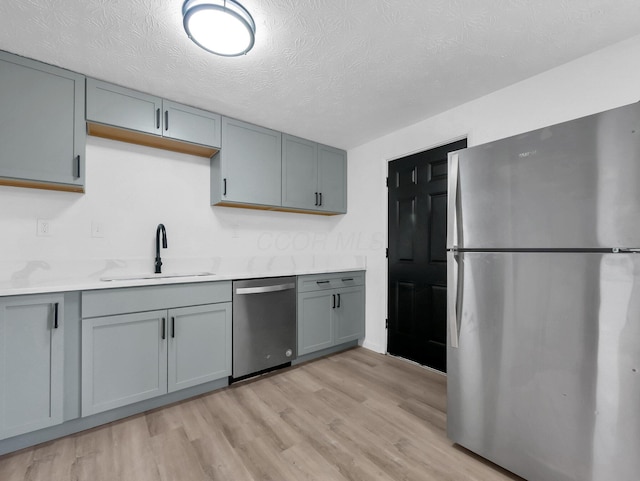 kitchen featuring stainless steel appliances, a sink, light wood finished floors, light countertops, and a textured ceiling