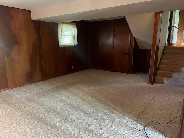 below grade area featuring carpet floors, wooden walls, and stairway