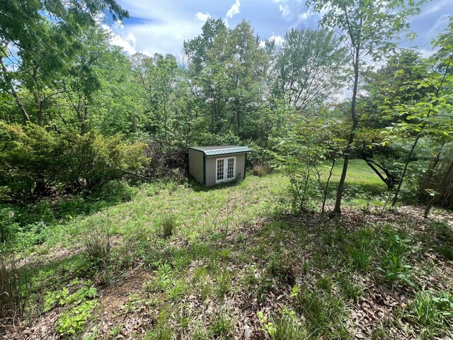 view of yard with an outdoor structure, french doors, and a wooded view