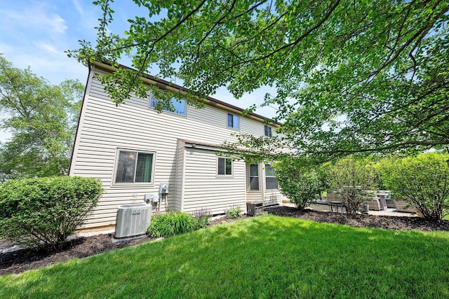 rear view of house featuring central air condition unit and a lawn