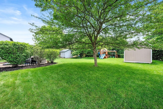 view of green lawn featuring a storage shed, a playground, and an outbuilding