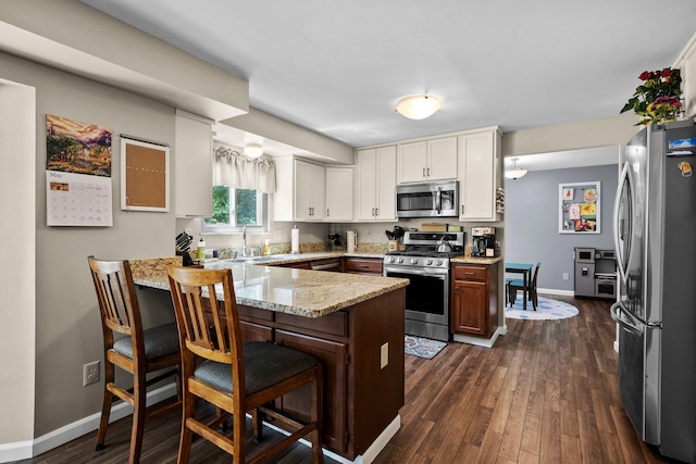kitchen featuring appliances with stainless steel finishes, a peninsula, baseboards, and dark wood-type flooring