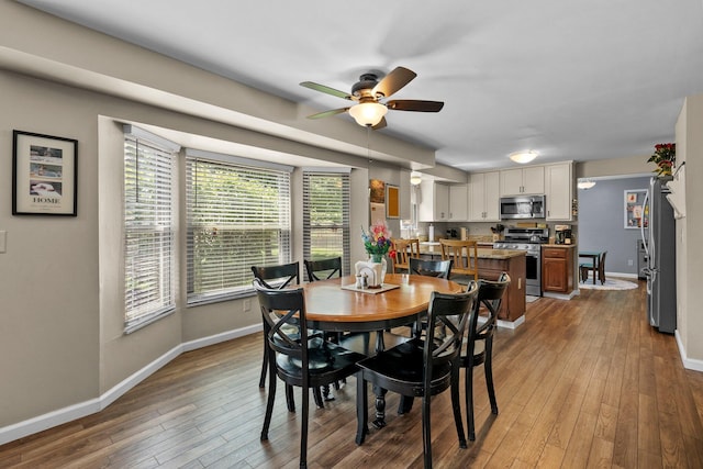 dining space with a ceiling fan, wood-type flooring, healthy amount of natural light, and baseboards