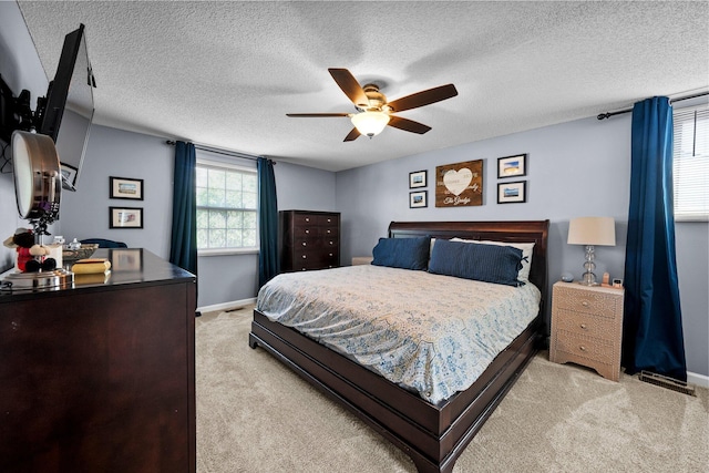 bedroom with light carpet, baseboards, a textured ceiling, and a ceiling fan