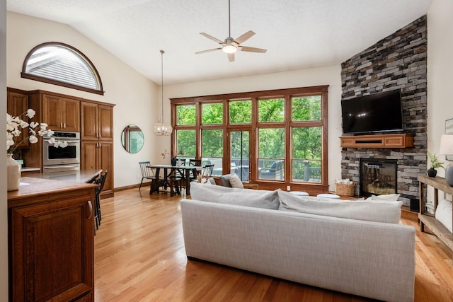 living area with a fireplace, a ceiling fan, light wood-type flooring, high vaulted ceiling, and baseboards