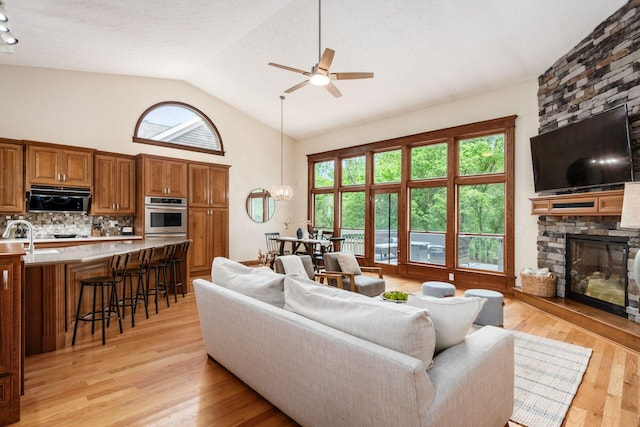 living room featuring ceiling fan, a fireplace, plenty of natural light, light wood finished floors, and high vaulted ceiling