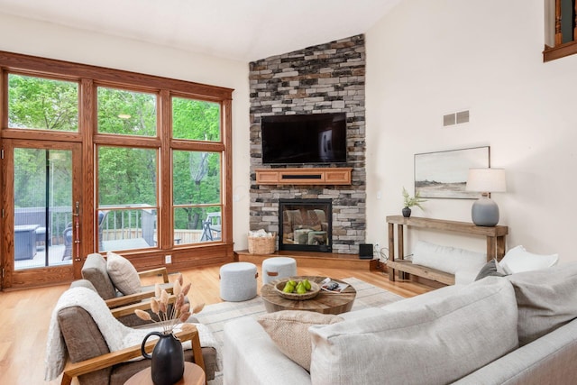 living room featuring a stone fireplace, wood finished floors, and high vaulted ceiling