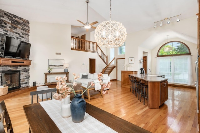 dining room featuring healthy amount of natural light, stairs, a stone fireplace, light wood finished floors, and high vaulted ceiling