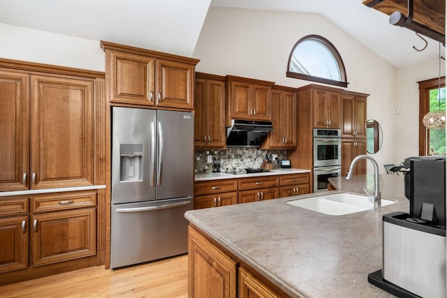 kitchen with stainless steel appliances, a sink, exhaust hood, vaulted ceiling, and brown cabinets