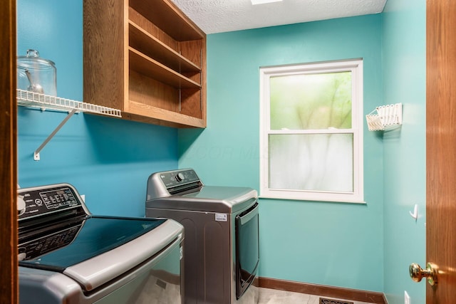 clothes washing area featuring washing machine and clothes dryer, baseboards, and a textured ceiling