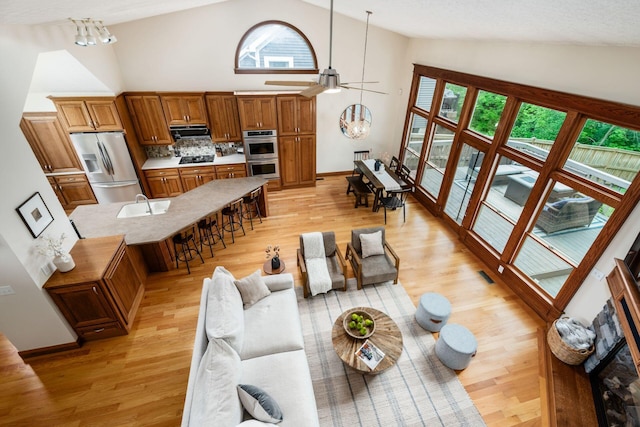 living room with high vaulted ceiling, plenty of natural light, light wood-style floors, a ceiling fan, and baseboards