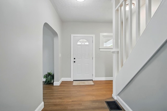 foyer entrance featuring arched walkways, baseboards, wood finished floors, a textured ceiling, and stairs