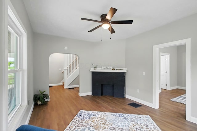 living area with wood finished floors, a ceiling fan, arched walkways, baseboards, and a brick fireplace