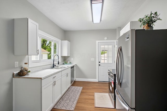 kitchen with appliances with stainless steel finishes, a sink, light wood finished floors, light countertops, and white cabinetry