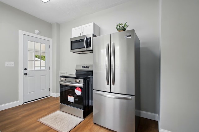 kitchen with appliances with stainless steel finishes, wood finished floors, baseboards, and white cabinets