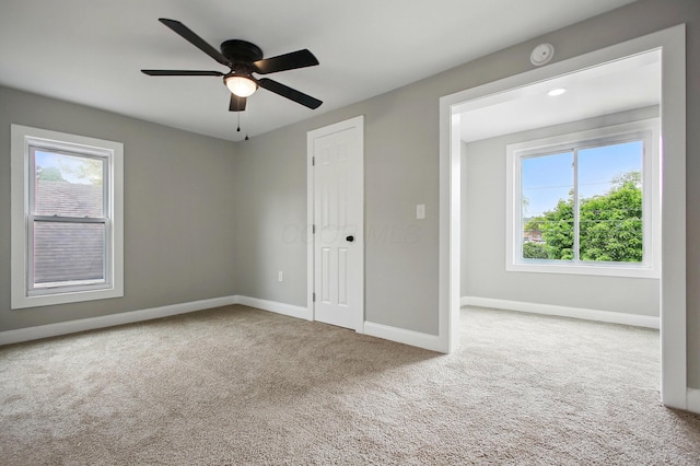 unfurnished bedroom with carpet flooring, multiple windows, baseboards, and a ceiling fan