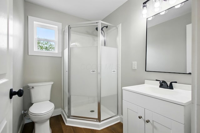 bathroom featuring wood finished floors, vanity, a shower stall, toilet, and baseboards