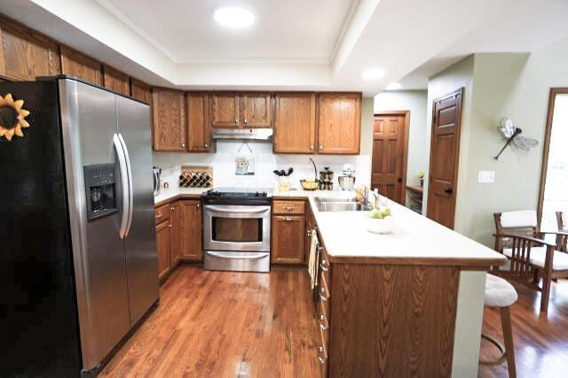 532 Woodview Rd, Westerville, OH 43081 - kitchen with stainless steel appliances, under cabinet range hood, a peninsula, wood finished floors, and brown cabinetry