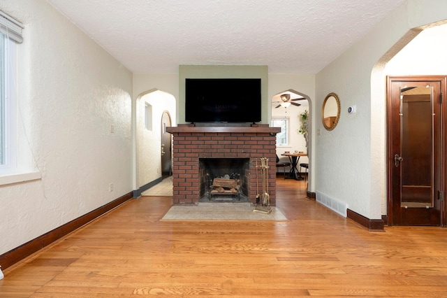 651 Eastern Ave, Bellefontaine, OH 43311 - living area featuring arched walkways, a textured wall, a textured ceiling, a fireplace, and light wood-style flooring