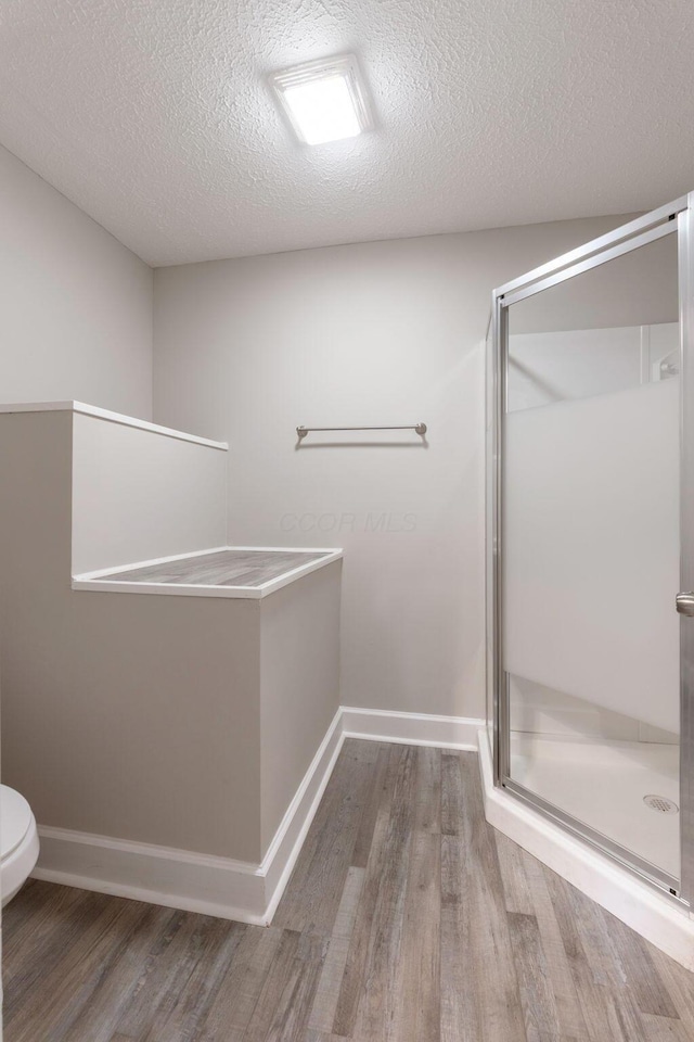 581 Kelton Ave, Columbus, OH 43205 - bathroom with wood finished floors, a shower stall, a textured ceiling, toilet, and baseboards