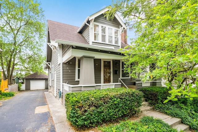 view of front of house featuring asphalt driveway, a detached garage, a porch, an outbuilding, and a shingled roof