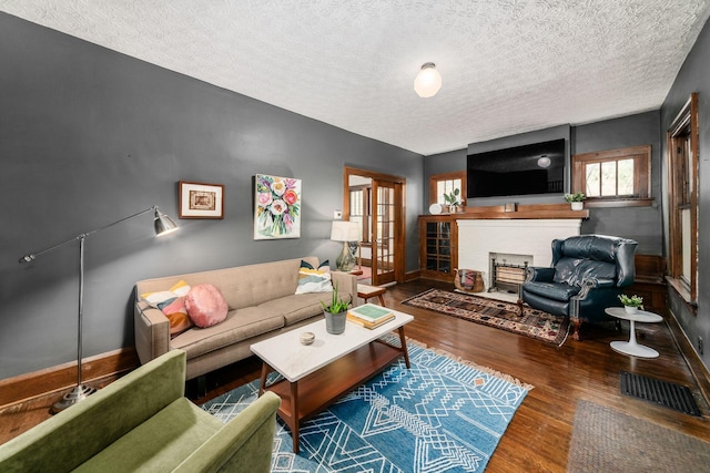 living room featuring wood finished floors, a fireplace with flush hearth, a textured ceiling, and baseboards