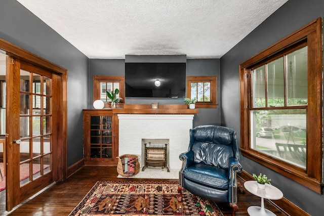 living area featuring baseboards, wood-type flooring, a textured ceiling, and a fireplace