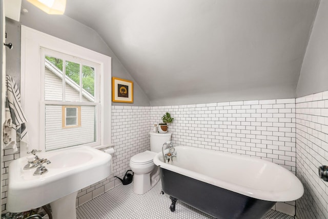 bathroom with lofted ceiling, a freestanding tub, toilet, a sink, and tile walls