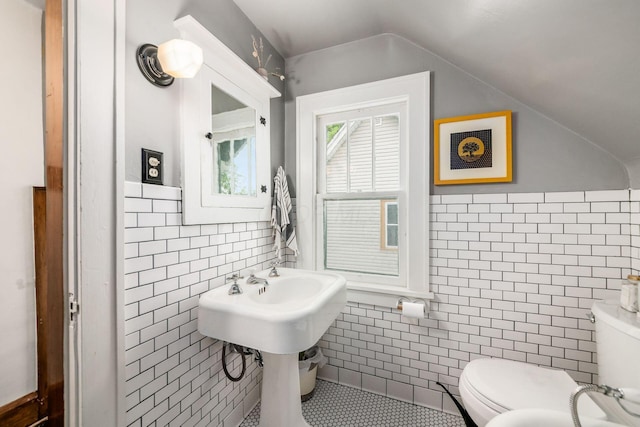 bathroom with tile walls, toilet, vaulted ceiling, tile patterned flooring, and a wainscoted wall