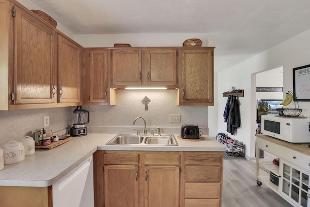 kitchen featuring white appliances, a sink, light countertops, and light wood-style flooring