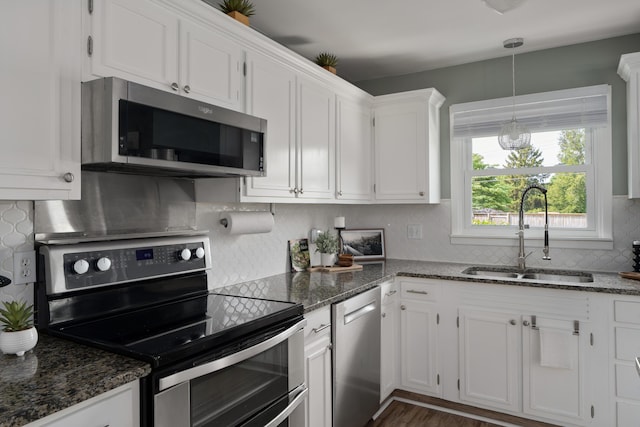 6235 George Fox Dr, Galloway, OH 43119 - kitchen featuring appliances with stainless steel finishes, white cabinetry, tasteful backsplash, dark stone counters, and decorative light fixtures