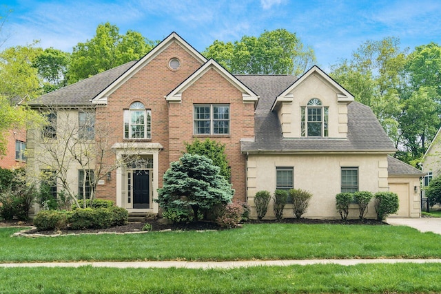 view of front of home featuring roof with shingles, a front yard, stucco siding, and brick siding