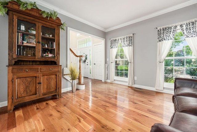 foyer with crown molding, baseboards, and light wood-style floors