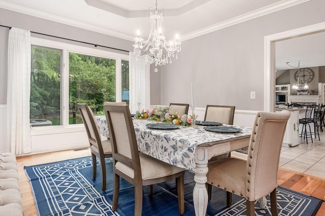 dining area with a chandelier, light wood-style flooring, a tray ceiling, and ornamental molding