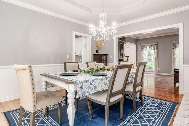 dining area featuring wood finished floors, a chandelier, a tray ceiling, ornamental molding, and baseboards