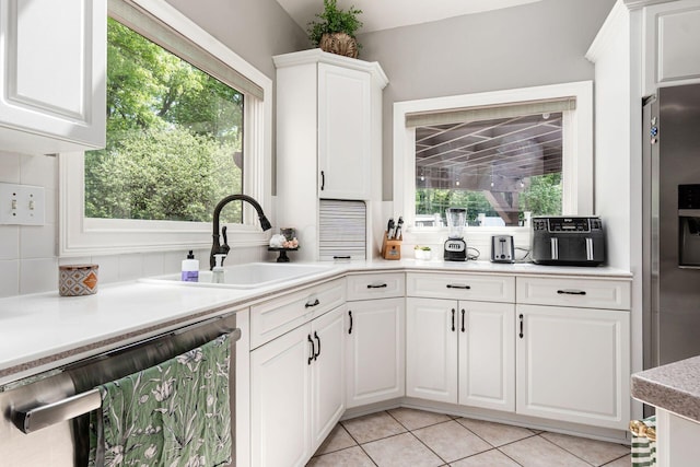 kitchen featuring appliances with stainless steel finishes, a sink, decorative backsplash, white cabinets, and light countertops
