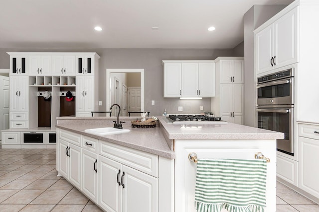 kitchen featuring a sink, stainless steel appliances, light tile patterned flooring, a center island with sink, and white cabinetry