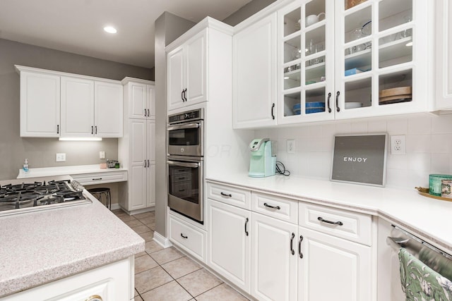 kitchen featuring appliances with stainless steel finishes, light tile patterned floors, white cabinetry, glass insert cabinets, and light countertops