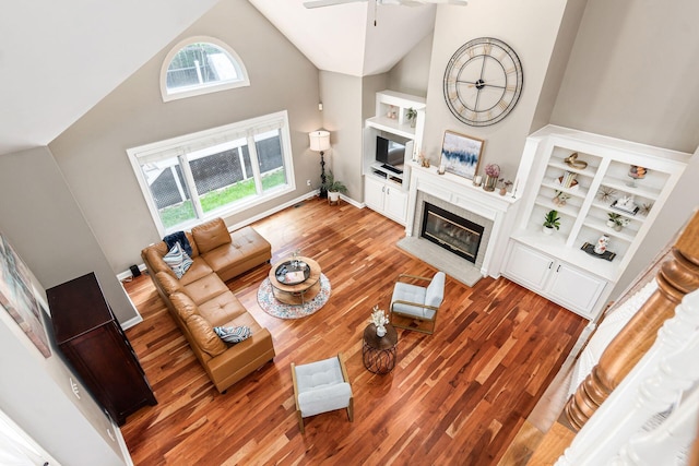 living area featuring high vaulted ceiling, a glass covered fireplace, ceiling fan, and wood finished floors