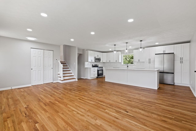 unfurnished living room with recessed lighting, light wood-style flooring, baseboards, a sink, and stairway