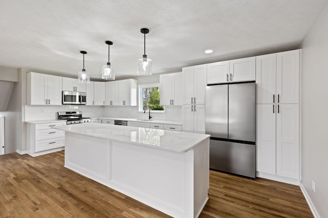 kitchen with appliances with stainless steel finishes, a sink, a kitchen island, white cabinetry, and backsplash