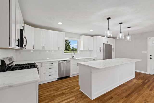 kitchen featuring appliances with stainless steel finishes, a sink, a center island, decorative backsplash, and wood finished floors