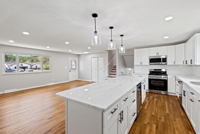 kitchen with stainless steel appliances, light wood-type flooring, recessed lighting, a center island, and light stone counters