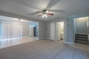 unfurnished living room with a ceiling fan, baseboards, carpet floors, and stairway