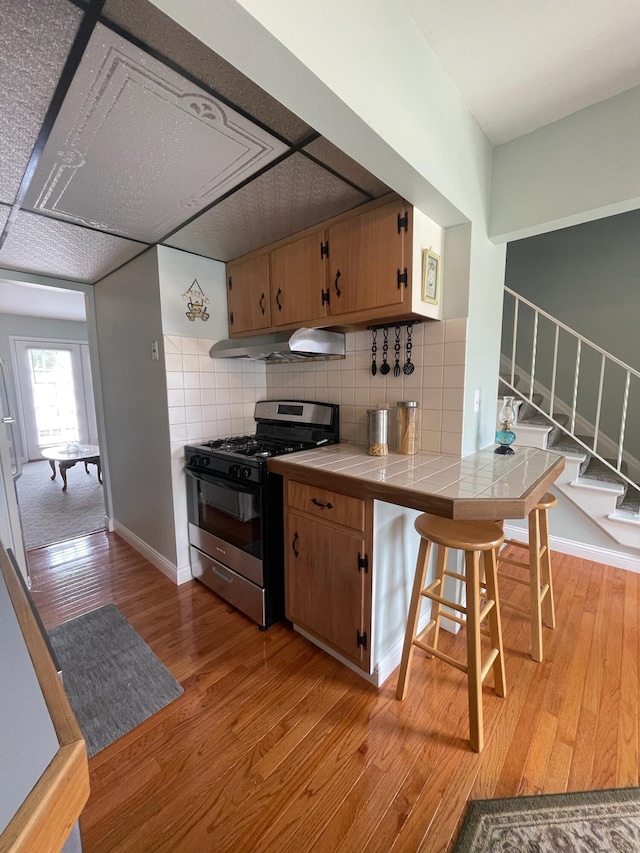 137 Tarryton Ct W Unit 24H, Columbus, OH 43228 - kitchen with gas range, tile countertops, light wood finished floors, under cabinet range hood, and backsplash